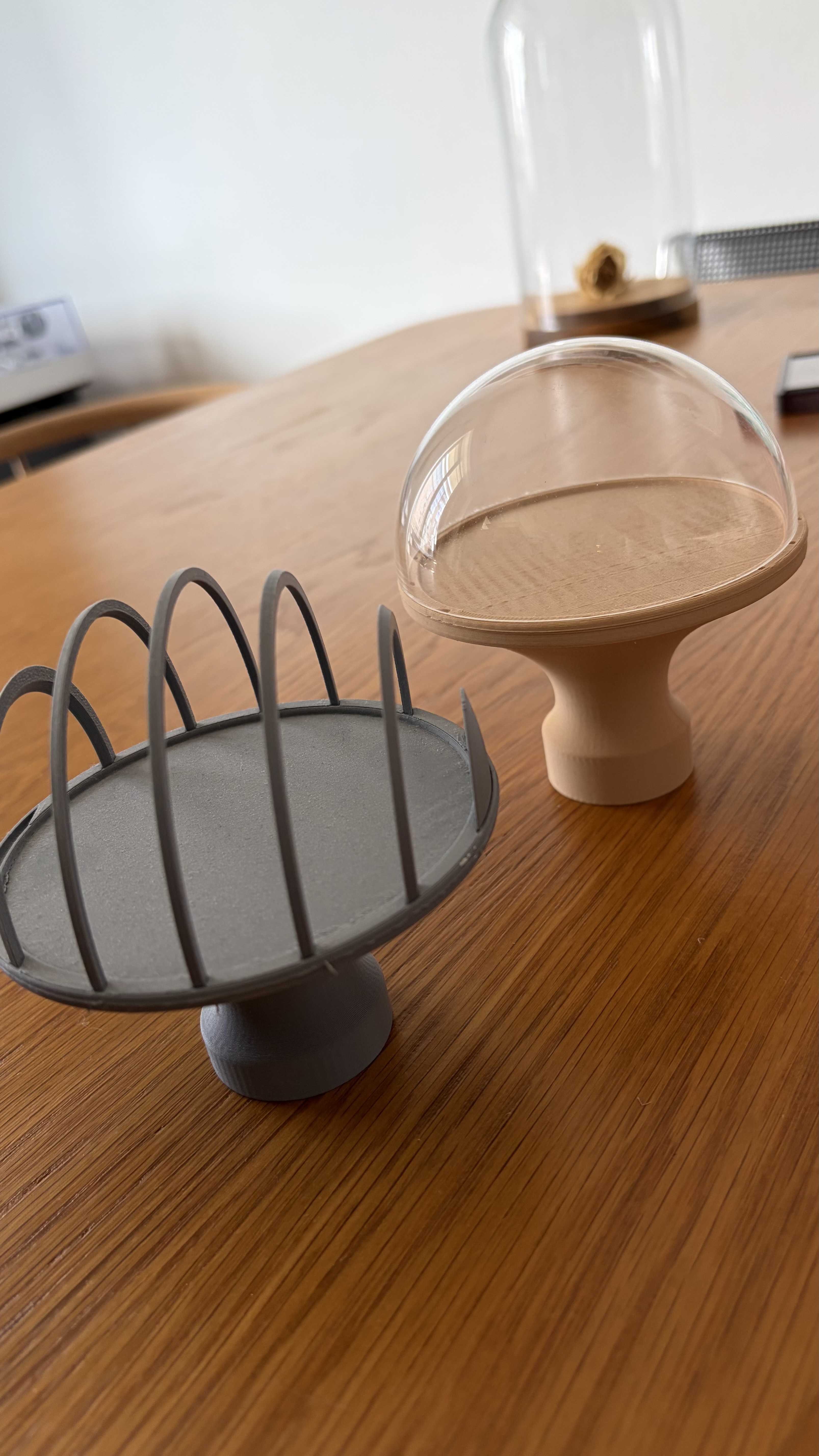 Two 3D-printed Dome prototypes on a wooden table, one in grey PLA with a ribbed shell and one in wood-toned PLA with the acrylic dome fitted